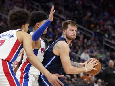 Dallas Mavericks guard Luka Doncic (77) looks to pass as Detroit Pistons guard Killian Hayes, center, and guard Cade Cunningham (2) defend during the second half of an NBA basketball game, Wednesday, April 6, 2022, in Detroit. (AP Photo/Carlos Osorio)