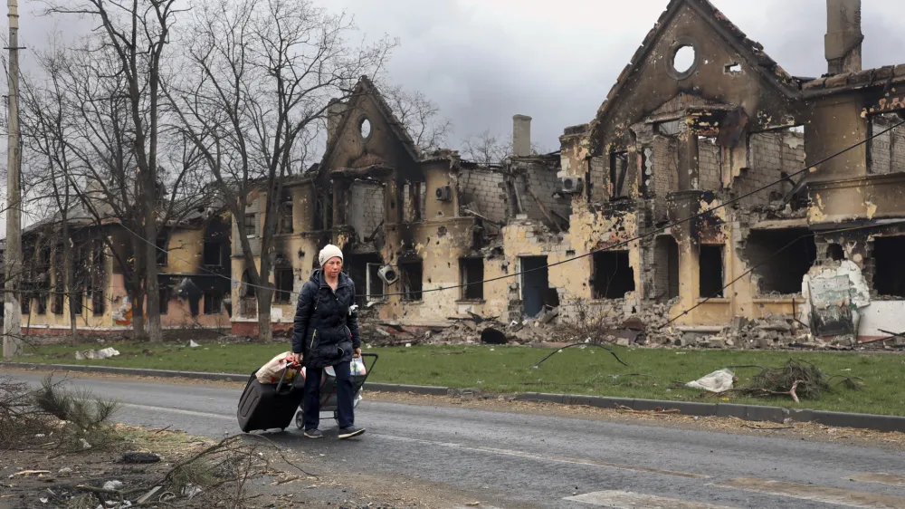 A woman pulls her bags past houses damaged during a fighting in Mariupol, on the territory which is now under the Government of the Donetsk People's Republic control, eastern in Mariupol, Ukraine, Friday, April 8, 2022. (AP Photo/Alexei Alexandrov)
