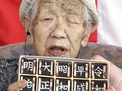 In this Monday, April 1, 2019, photo, Kane Tanaka, who is honored as the world's oldest living person by Guinness World Records at 116, poses with chocolates with era names at a nursing home in Fukuoka, southwestern Japan. Tanaka was born in Meiji era, and will soon experience the fifth era, starting on May 1. The words, from left, read "Meiji, Taisho, Showa, Heisei and Reiwa." (Ryosuke Uematsu/Kyodo News via AP)