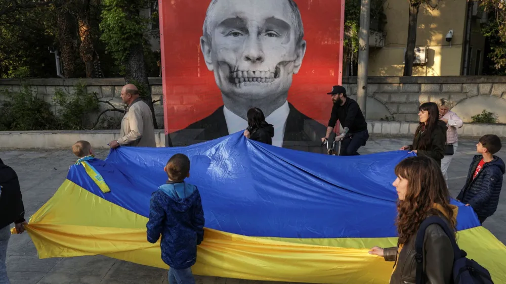 Protesters carrying a large Ukrainian flag and heading to a protest against Russia's war in Ukraine, walk by a mesh depicting an artistic view of Vladimir Putin's portrait, featured in an anti-war exhibition near the Russian Embassy, in Bucharest, Romania, April 30, 2022. Inquam Photos/Octav Ganea via REUTERS ATTENTION EDITORS - THIS IMAGE WAS PROVIDED BY A THIRD PARTY. ROMANIA OUT. NO COMMERCIAL OR EDITORIAL SALES IN ROMANIA