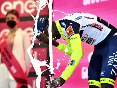 Eritrea's Biniam Girmay touches his eye after spraying sparkling wine on the podium to celebrate winning the 10th stage of the Giro D'Italia cycling race from Pescara to Jesi, Italy, Tuesday, May 17, 2022. Girmay was then taken to a local hospital after getting injured when he popped a champagne cork into his eye during the podium celebration. (Massimo Paolone/LaPresse via AP)