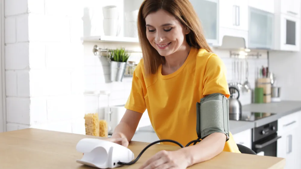Woman checking blood pressure with sphygmomanometer at table indoors. Cardiology concept