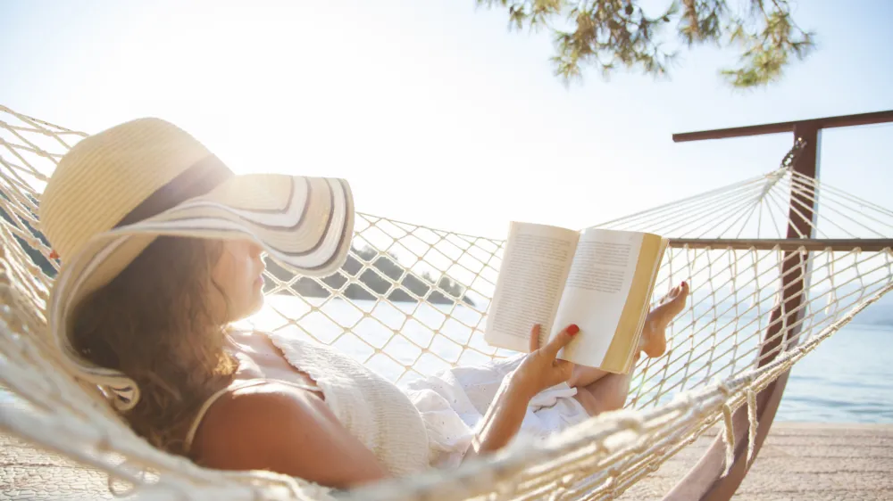 Woman in a hammock with book on summer day