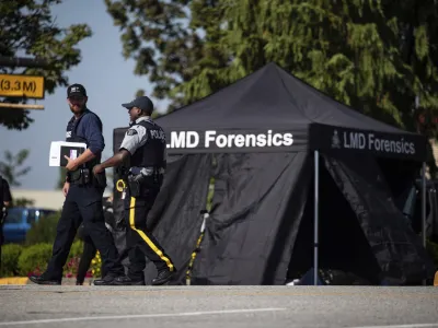 RCMP officers talk as a tent covers a body at the scene of a shooting in Langley, British Columbia, Monday, July 25, 2022. Canadian police reported multiple shootings of homeless people Monday in a Vancouver suburb and said a suspect was in custody. (Darryl Dyck/The Canadian Press via AP)
