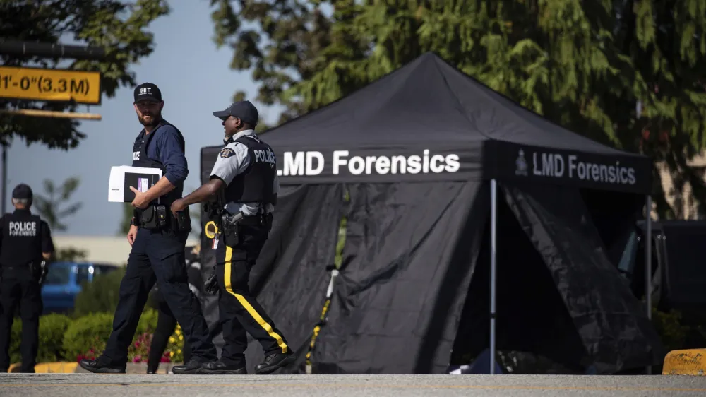 RCMP officers talk as a tent covers a body at the scene of a shooting in Langley, British Columbia, Monday, July 25, 2022. Canadian police reported multiple shootings of homeless people Monday in a Vancouver suburb and said a suspect was in custody. (Darryl Dyck/The Canadian Press via AP)