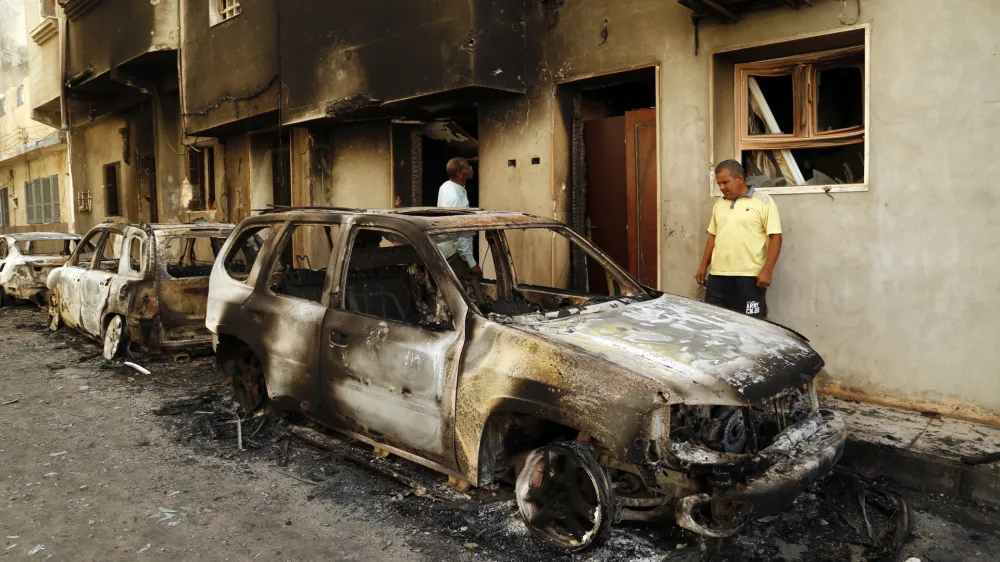 Men survey the remains of cars burned during clashes on a street in the Libyan capital of Tripoli, Sunday, August 28 2022. Deadly clashes broke out Saturday in Libya's capital between militias backed by its two rival administrations, portending a return to violence amid a long political stalemate. (AP Photo/Yousef Murad)