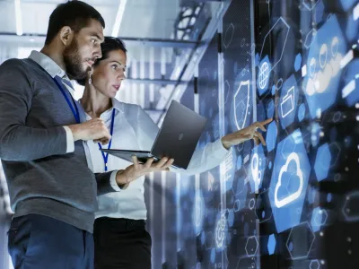 Male IT Specialist Holds Laptop and Discusses Work with Female Server Technician. They're Standing in Data Center, Rack Server Cabinet with Cloud Server Icon and Visualization.
