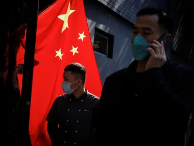 People wearing masks walk past a Chinese national flag as outbreaks of coronavirus disease (COVID-19) continue in Beijing, China, November 3, 2022. REUTERS/Thomas Peter