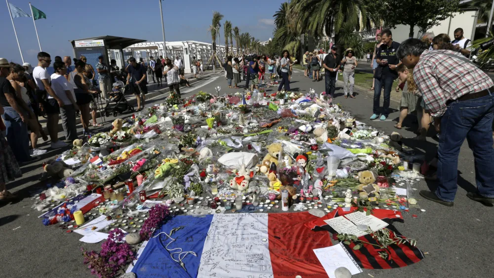 FILE - People look at flowers placed on the Promenade des Anglais at the scene of a truck attack Monday July 18, 2016 in Nice, southern France. A French court on Tuesday Dec.13, 2022 convicted eight people charged in connection with a truck attack more than six years ago by an Islamic State sympathizer that killed 86 people celebrating Bastille Day in the French Riviera city of Nice. (AP Photo/Claude Paris, File)