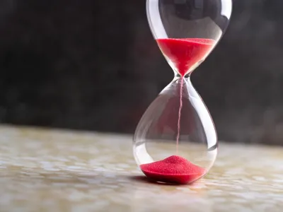 Sand passes through hourglass bulbs measuring the transit time counting down to the deadline, against a dark background
