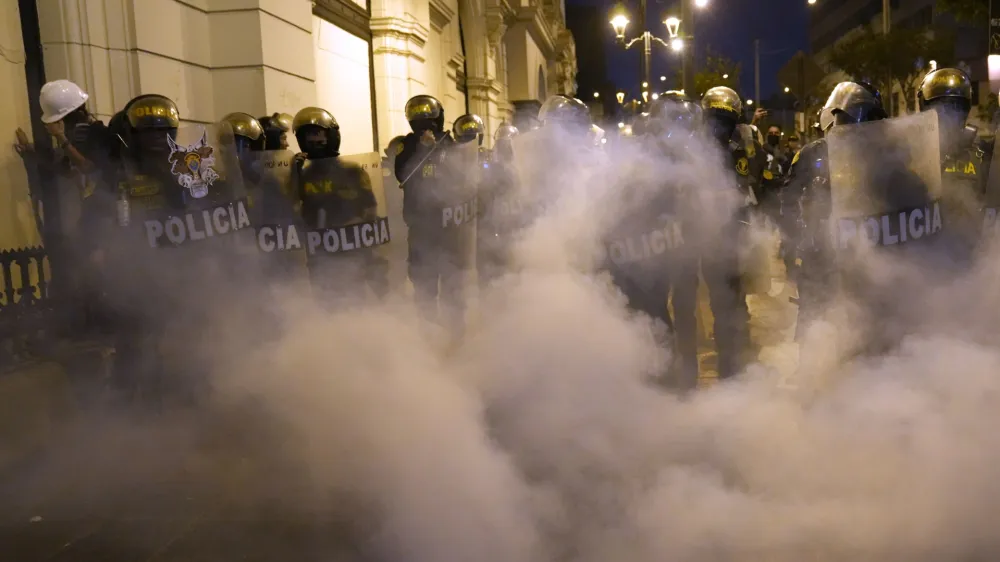 Riot police officers stand guard before clouds of tear gas after clashes with supporters of ousted Peruvian President Pedro Castillo, in Lima, Peru, Thursday, Dec. 15, 2022. A Peruvian judge on Thursday ordered Castillo to remain in custody for 18 months, approving a request from authorities for time to build their rebellion case against him. (AP Photo/Martin Mejia)
