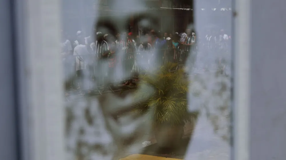Soccer Football - Death of Brazilian soccer legend Pele - Vila Belmiro Stadium, Santos, Brazil - January 2, 2023 Mourners queuing to pay their respect to Brazilian soccer legend Pele are seen in the reflection on a portrait of Pele hanging outside a house near his former club Santos' Vila Belmiro stadium REUTERS/Ricardo Moraes