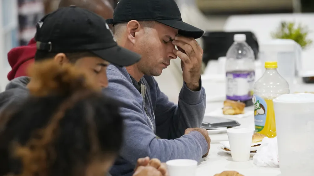 Roberto Sotolongo prays after dinner at the Iglesia Rescate, Tuesday, Feb. 21, 2023, in Hialeah, Fla. Sotolongo, from Havana, Cuba, crossed the U.S. Mexican border into the U.S. in November, leaving behind his wife and children. Sotolongo, a carpenter by trade, finds himself in limbo without a work permit to sustain himself and help his family in Cuba. (AP Photo/Marta Lavandier)