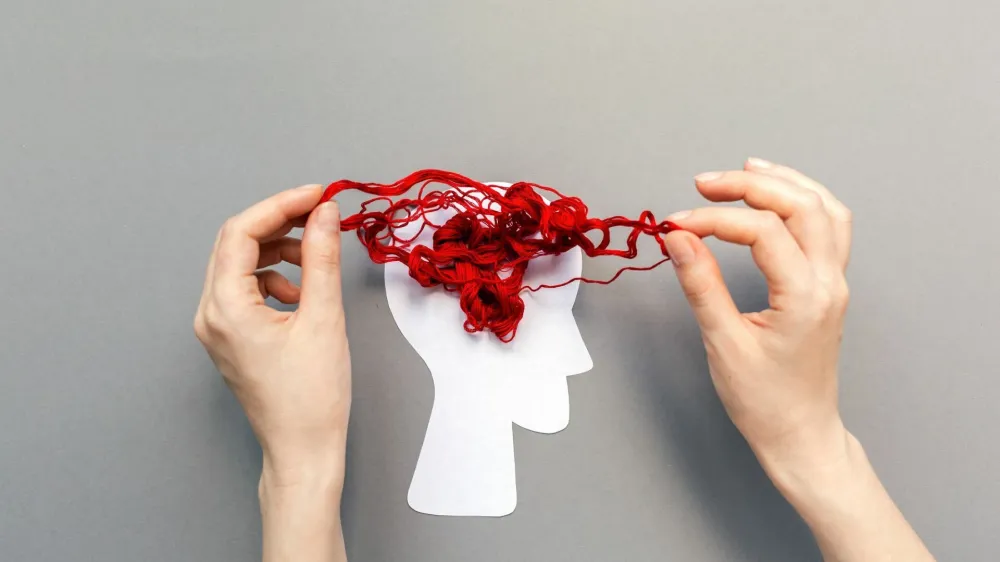 Tangled red threads on the silhouette of the head, representing the brain. Blue background. Flat lay. The concept of mental health and demension