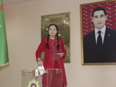 A woman wearing a national costume casts her ballot at a polling station with a portrait of President Serdar Berdymukhamedov, who was elected last year to succeed his father who had run the isolated ex-Soviet country for more than a decade in Ashgabat, Turkmenistan, Sunday, March 26, 2023. Voters in Turkmenistan have cast ballots for a new parliament that is expected to be opposition-free and loyal to the government of the gas-rich Central Asian nation. Sunday's election for 125 members included 258 candidates, put forward by three political parties or running independently. (AP Photo/Alexander Vershinin)