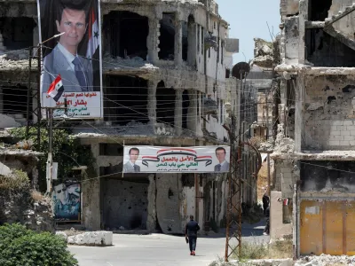 FILE PHOTO: A man walks past banners depicting Syria's President Bashar al-Assad, near damaged buildings, ahead of the May 26 presidential election, in Homs, Syria May 23, 2021. REUTERS/Omar Sanadiki/File Photo