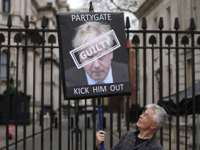 FILE - A protester holds a sign showing British Prime Minister Boris Johnson as he stands in front of the entrance to Downing Street in London, Wednesday, April 13, 2022. Former Prime Minister Boris Johnson deliberately misled Parliament about the lockdown-flouting parties that undermined his credibility and contributed to his downfall, a committee of lawmakers said Thursday, June 15, 2023 after a year-long investigation. (AP Photo/Frank Augstein, File)