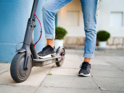 Close up on woman legs feet standing on the electric kick scooter on the pavement wearing jeans and sneakers in summer day