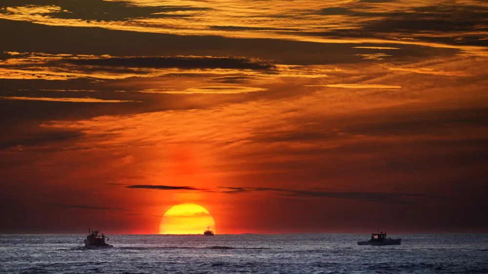 FILE - The sun rises over fishing boats in the Atlantic Ocean, Sept. 8, 2022, off of Kennebunkport, Maine. A system of ocean currents that carries heat northward across the North Atlantic could collapse during this century, according to a new study, and scientists have said before such a collapse could cause catastrophic sea-level rise and extreme weather across the globe. (AP Photo/Robert F. Bukaty, File)
