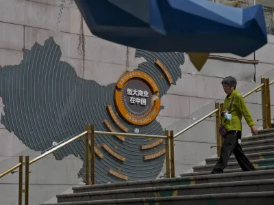 A woman walks by a map showing Evergrande development projects in China, as she heads to an Evergrande city plaza in Beijing, Monday, Sept. 18, 2023. Police in a southern Chinese city said on last Saturday they have detained some staff at China Evergrande Group's wealth management unit in the latest trouble for the heavily indebted developer. (AP Photo/Andy Wong)