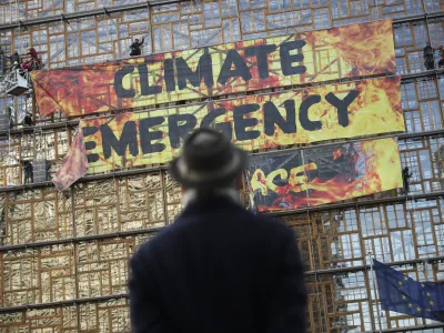 A man looks up as police and fire personnel move in to remove climate activists after they climbed the Europa building during a demonstration outside an EU summit meeting in Brussels, Thursday, Dec. 12, 2019. Greenpeace activists on Thursday scaled the European Union's new headquarters, unfurling a huge banner warning of a climate emergency hours before the bloc's leaders gather for a summit focused on plans to combat global warming.(AP Photo/Francisco Seco)