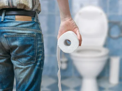 Man suffers from diarrhea holds toilet paper roll in front of toilet bowl.