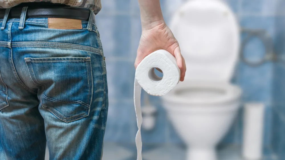 Man suffers from diarrhea holds toilet paper roll in front of toilet bowl.