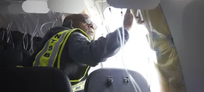 This image taken Sunday, Jan. 7, 2024, and released by the National Transportation Safety Board, an investigator examines the frame on a section of Alaska Airlines Flight 1282 that is missing panel on a Boeing 737-9 MAX in Portland, Ore. Federal officials are investigating Boeing's oversight of production of a panel that blew off a jetliner in midflight last week. (NTSB via AP) 