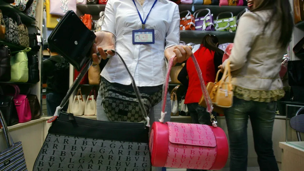 A sales clerk wearing a fanny pack with a Gucci label displays handbags bearing the Bulgari trademark name, as other bags showing the Yves Saint Laurent brand are seen behind, in Beijing's newly opened Silk Market commercial plaza Thursday March 31, 2005. Earlier this week inspectors confiscated more than 300 items in a raid on faked or pirated goods in the market. Responding to a new U.S. report that complains of "epidemic levels" of counterfeiting, China on Thursday insisted it is aggressively fighting the problem to protect both Chinese and foreign companies. (AP Photo/Elizabeth Dalziel)