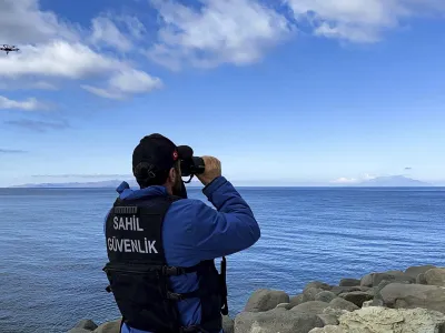 A member of Turkish Coastal Security uses binoculars on the Turkey's shore of Aegean sea in Eceabat, Turkey, Friday, March 15, 2024. A rubber dinghy carrying migrants sank off Turkey's northern Aegean coast on Friday, killing at least 22 people, officials said. (Dia Images via AP)