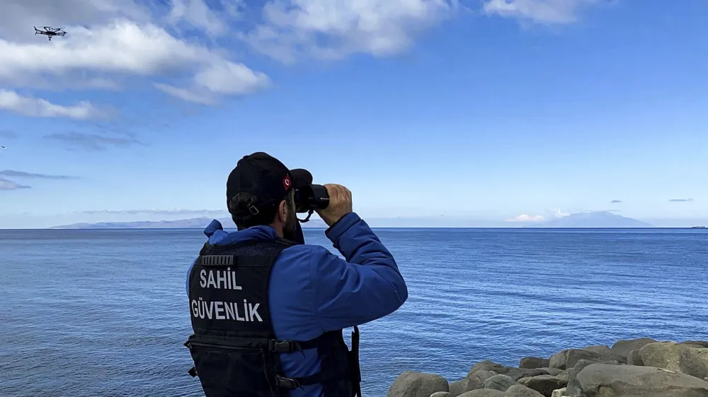 A member of Turkish Coastal Security uses binoculars on the Turkey's shore of Aegean sea in Eceabat, Turkey, Friday, March 15, 2024. A rubber dinghy carrying migrants sank off Turkey's northern Aegean coast on Friday, killing at least 22 people, officials said. (Dia Images via AP)