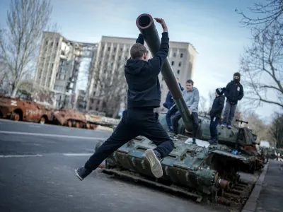 FILED - 25 February 2024, Ukraine, Mykolaiv: Children play on a destroyed Russian tank in front of the former headquarters of the regional administration of Mykolaiv oblast, after the visit of the German Foreign Minister. On March 29, 2022, the building was hit by Russian missiles and almost completely destroyed. Mykolaiv is an important port city near Odessa. Photo: Kay Nietfeld/dpa