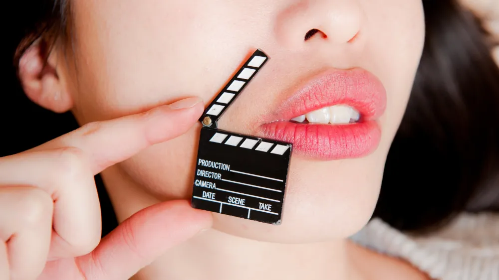 Face detail of sensual woman lips, no eyes, with hand holding little movie clapper board