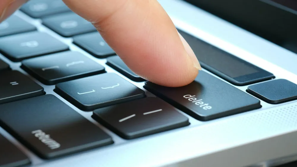 Finger of the computer user, he presses the delete button on the computer keyboard.