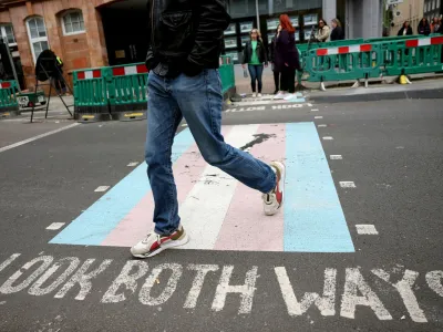 A person walks on a pedestrian crossing decorated with the pattern of the transgender flag on a street in London, Britain, April 10, 2024. REUTERS/Isabel Infantes