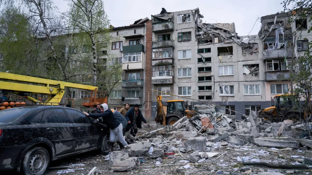 14 April 2023, Ukraine, Sloviansk: Residents push a damaged car in front of a damaged building in Sloviansk. Russian troops attacked eastern Ukrainian city Sloviansk on eastern Orthodox great Friday, causing at least 8 dead and 21 injured, including children and many buildings destroyed. Photo: Ashley Chan/SOPA Images via ZUMA Press Wire/dpa