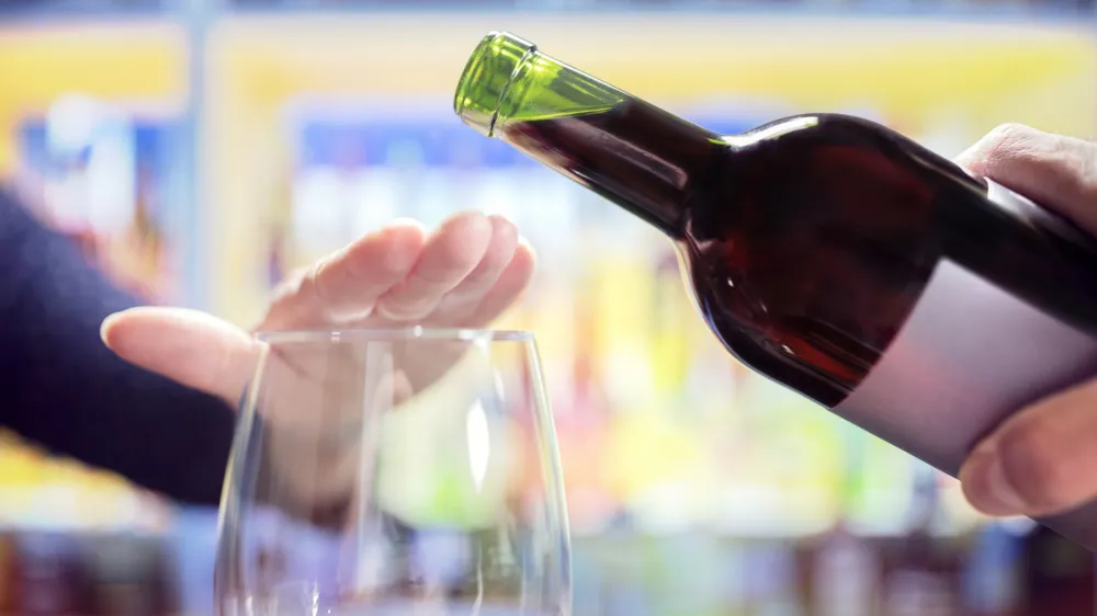 Womans hand rejecting more alcohol from wine bottle in bar