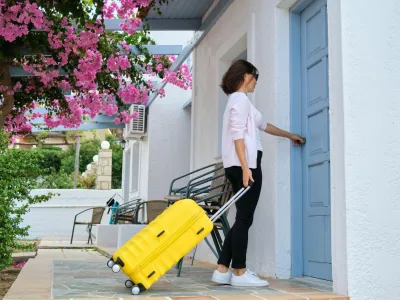 Tourism, travel, resort, vacation, rental of real estate, accommodation in a villa. Outdoor, woman traveler with yellow suitcase opening closing door of the house