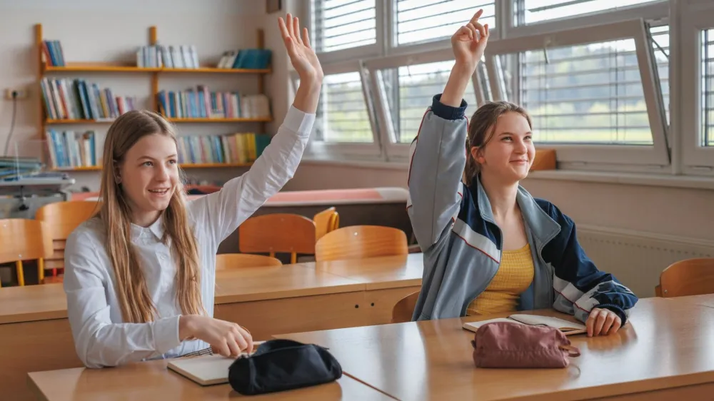 Two teen female pupils raising their hands to answer the question in the classroom. Back to school concept.