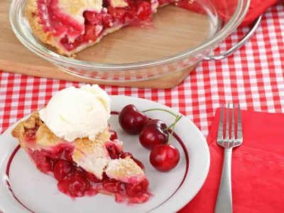 Slice of cherry pie with a scoop of ice cream on a plate