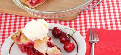 Slice of cherry pie with a scoop of ice cream on a plate