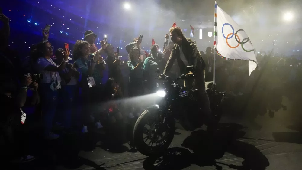 Tom Cruise rides a motorbike with the Olympic flag attached during the 2024 Summer Olympics closing ceremony at the Stade de France, Sunday, Aug. 11, 2024, in Saint-Denis, France. (AP Photo/Ashley Landis)