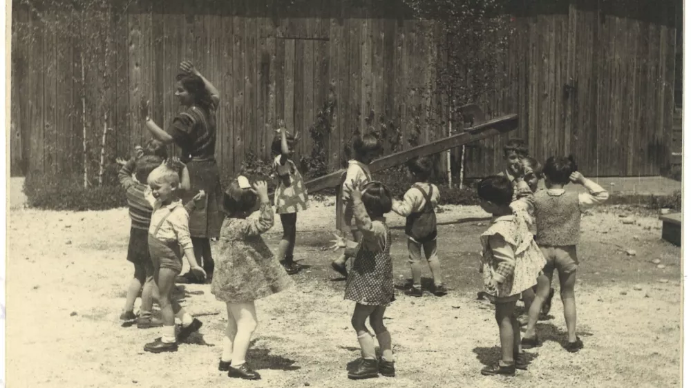 Vrtec Prule, malčki z vzgojiteljico Savico Lanc leta 1956 nastopajo na igri&scaron;ču pred vrtcem, barako. Ple&scaron;ejo in predstavljajo medvedke. SI_ZAL_LJU/0840, Vzgojno-varstvena organizacija Prule. 