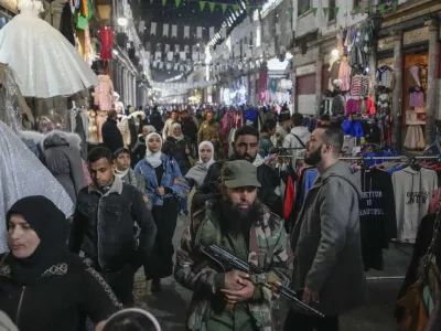 An armed opposition fighter walks among costumers at the Al-Hamidiyeh market inside the old walled city of Damascus, Syria, Tuesday, Dec. 10, 2024. (AP Photo/Hussein Malla)