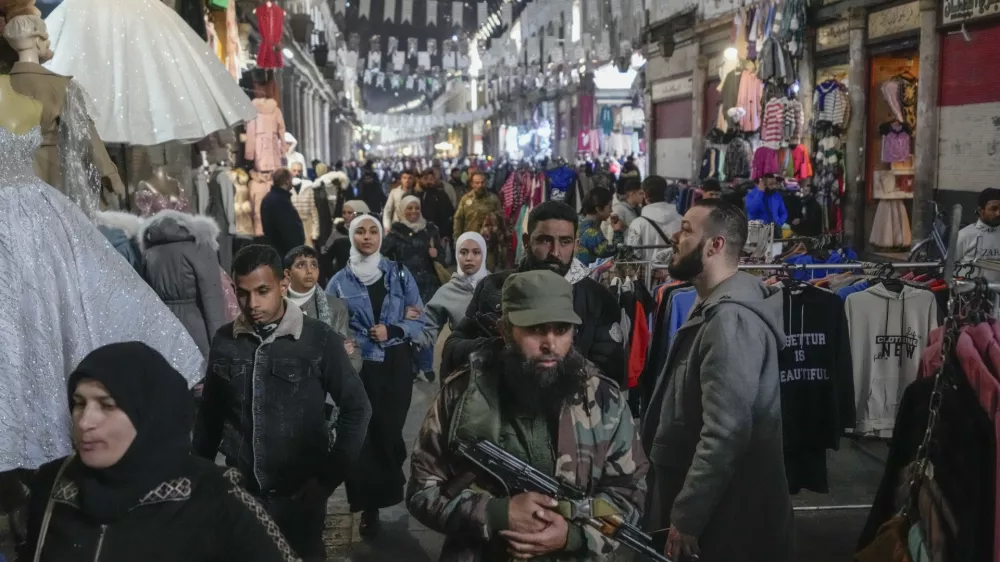 An armed opposition fighter walks among costumers at the Al-Hamidiyeh market inside the old walled city of Damascus, Syria, Tuesday, Dec. 10, 2024. (AP Photo/Hussein Malla)