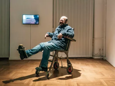 Tomaž Furlan demonstrira eno od svojih intermedijskih zamisli, po kateri se z brco mehanski voziček premakne naprej; pregledna razstava Mati vseh bojev v Mestni galeriji Ljubljana. Foto: Blaž Gutman