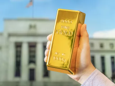 a gold bar in a man's hand against the background of the central bank, US Federal Reserve system. / Foto: Diy13