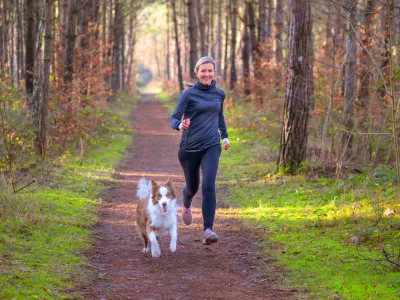Healthy fit woman running with her dog jogging together through a forest along a footpath approaching the camera with a happy smile / Foto: Mheim3011