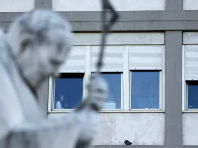 People are seen near a window as the statue of late Pope John Paul II stands outside Gemelli Hospital, where Pope Francis is admitted for treatment, in Rome, Italy, February 27, 2025. REUTERS/Yara Nardi