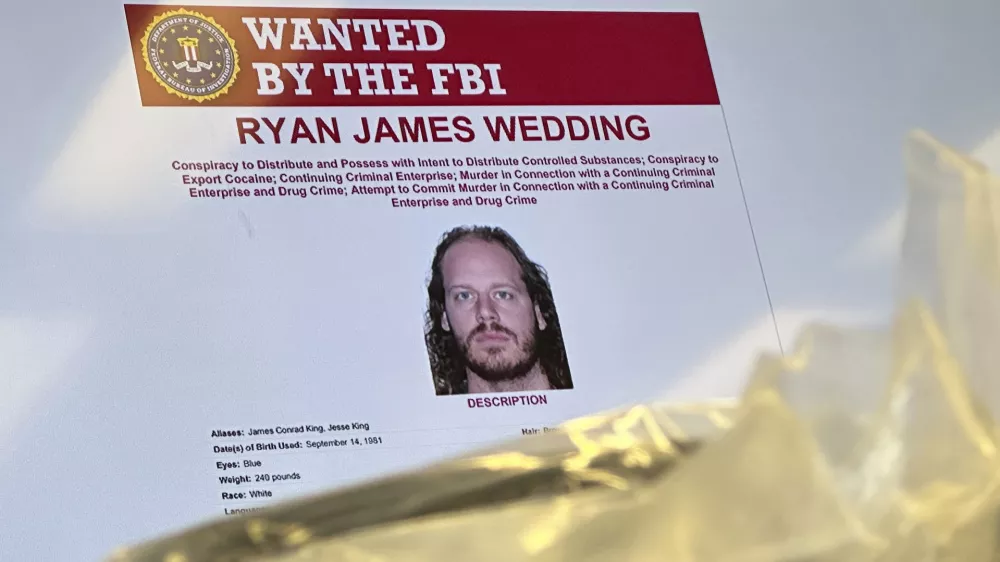 An image of former Canadian Olympic snowboarder Ryan Wedding, 43, who is a fugitive and been charged with allegedly running and participating in a transnational drug trafficking operation, is displayed on a video monitor along with bricks of cocaine, foreground, during a news conference at the FBI offices in Los Angeles, Thursday, Oct. 17, 2024. (AP Photo/Damian Dovarganes)